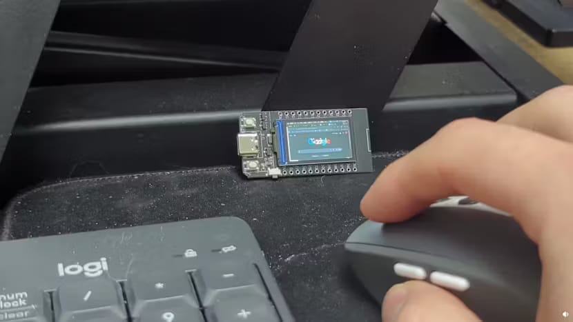 Esta foto muestra una pequeña pantalla de escritorio sobre una mesa con un teclado, un mouse y las manos visibles.